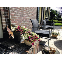 Terrass med trädgårdsmöbler, blomlådor och dekorationer framför en tegelvägg.