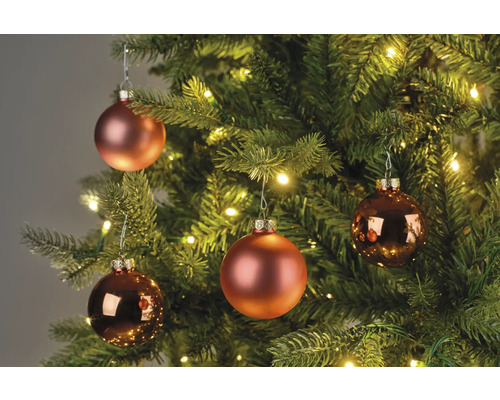 Närbild av julgranskulor i en julgran med belysning.