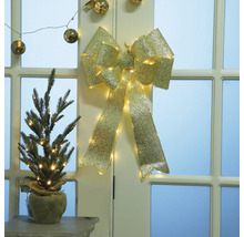 Dekorativ guldfärgad rosett med belysning och liten gran i jutesäck på bord framför dörr