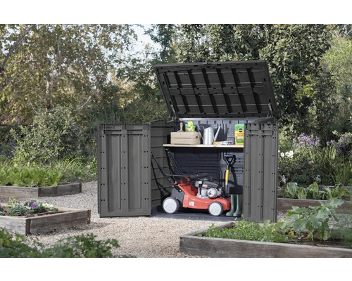 Trädgårdsskåp med öppet lock och dörr i trädgården, med gräsklippare och trädgårdsredskap