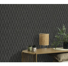 Närbild av en vägg med en strukturerad tapet, ett bord med en lampa och växter