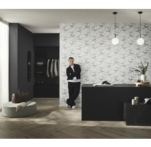 Rumsöversikt med mönstrad tapet, byrå, belysning och man