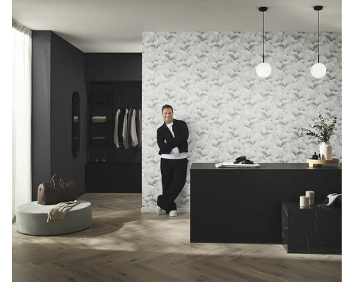 Rumsöversikt med mönstrad tapet, byrå, belysning och man