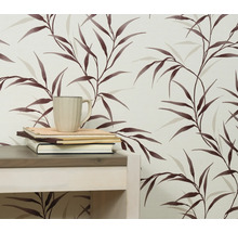 Närbild av en vägg med en tapet med bladmönster, ett bord, böcker och en kopp.