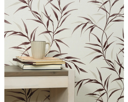 Närbild av en vägg med en tapet med bladmönster, ett bord, böcker och en kopp.