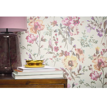 Närbild av en vägg med blommig tapet, kompletterad med en lampa, böcker och en skål på en trämöbel.
