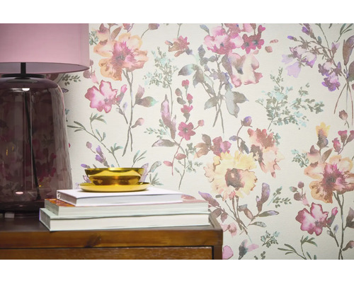 Närbild av en vägg med blommig tapet, kompletterad med en lampa, böcker och en skål på en trämöbel.