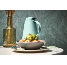 Dekorativt stilleben med vas, termos och fruktskål framför en tapet med bladmönster.