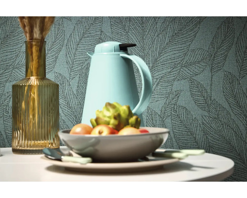 Dekorativt stilleben med vas, termos och fruktskål framför en tapet med bladmönster.