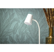 Närbild av en strukturerad tapet med bladmönster, en vit lampa och en vas med dekorativt gräs