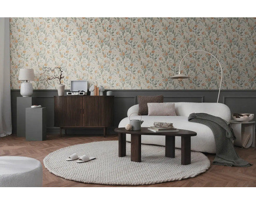 Vardagsrum med blommig tapet, soffa, matta och trämöbler för en mysig atmosfär.