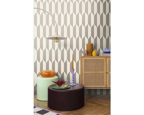 Vardagsrum med geometrisk tapet, lampa, byrå och dekorativa föremål för en stilfull inredning.