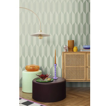 Dekorativt rum med geometrisk tapet, golvlampa, byrå och sidobord.