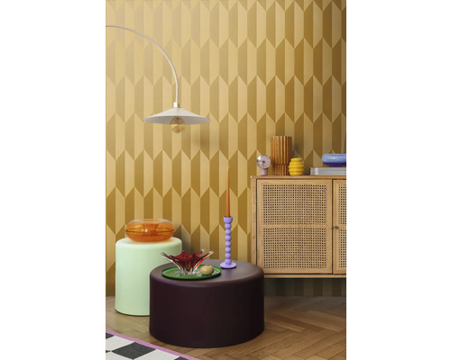 Inredningsexempel med en lampa, diverse bord och ett skåp framför en tapet med geometriskt mönster.