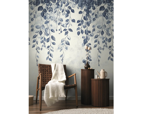 Dekorativ vägg med bladmönster, fåtölj med filt och sidobord i vardagsrummet.