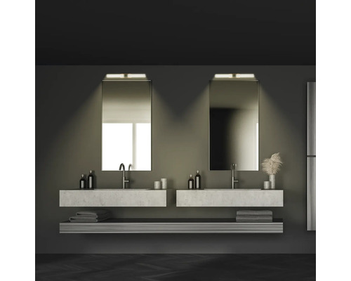 Badrum med två handfat, speglar, handdukar och hyllor i mörka toner.