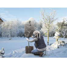 Kvinna fäster ett vinterskydd på en växt i trädgården