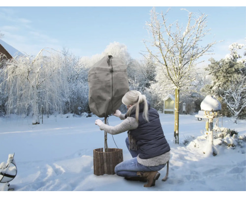Kvinna fäster ett vinterskydd på en växt i trädgården