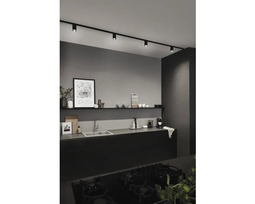 Modernt kök med svarta köksskåp, diskho, hylla och svart skensystem med spotlights.