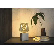 Dekorativ bordslampa med LED-lampa på ett nattduksbord bredvid böcker och en växt.