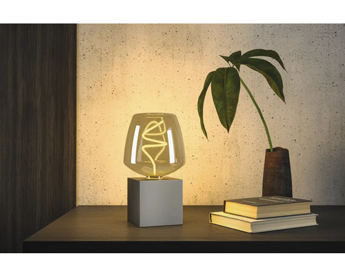 Dekorativ bordslampa med LED-lampa på ett nattduksbord bredvid böcker och en växt.