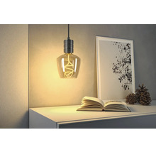 Dekorativ hänglampa med spiralformad glödtråd ovanför byrå med bok och bild