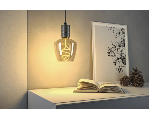 Dekorativ hänglampa med spiralformad glödtråd ovanför byrå med bok och bild