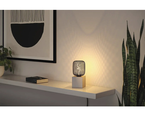 Dekorativ bordslampa med gallerstruktur och träfot på en hylla