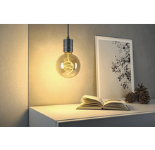 Dekorativ glödlampa med öppen spiral hänger ovanför en byrå med bok och bild