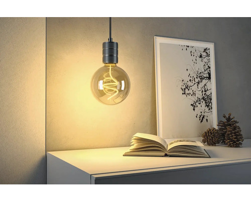 Dekorativ glödlampa med öppen spiral hänger ovanför en byrå med bok och bild