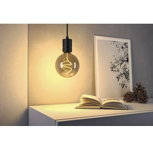 Dekorativ hänglampa ovanför en öppen bok, bredvid ett inramat foto och kottar på en byrå