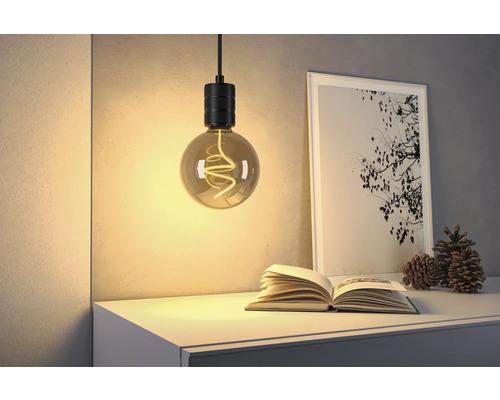 Dekorativ hänglampa ovanför en öppen bok, bredvid ett inramat foto och kottar på en byrå