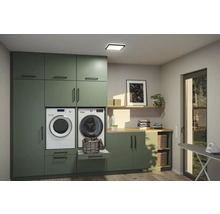 Modern tvättstuga med gröna skåp, tvättmaskin, torktumlare, hyllor och strykbräda.