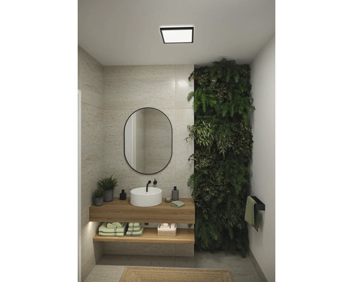 Modernt badrum med handfat, spegel, växtvägg och taklampa.