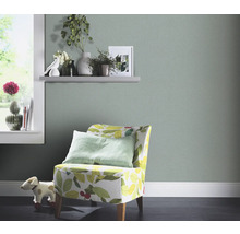 Vardagsrum med ljusgrön tapet, fåtölj med bladmönster och dekorationer på en hylla