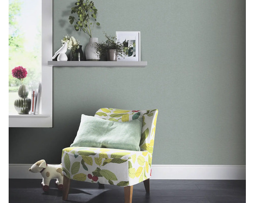 Vardagsrum med ljusgrön tapet, fåtölj med bladmönster och dekorationer på en hylla