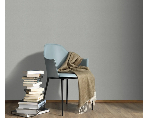 Scen med en stol, en filt och en hög med böcker mot en grå vägg.