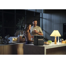 Ett par i ett kök med en bärbar strömgenerator som driver en lampa medan en mikrovågsugn går i bakgrunden.