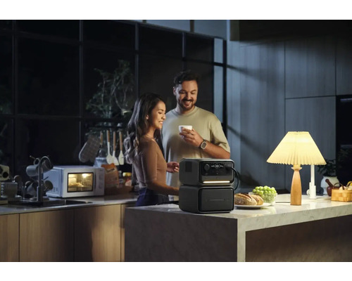 Ett par i ett kök med en bärbar strömgenerator som driver en lampa medan en mikrovågsugn går i bakgrunden.