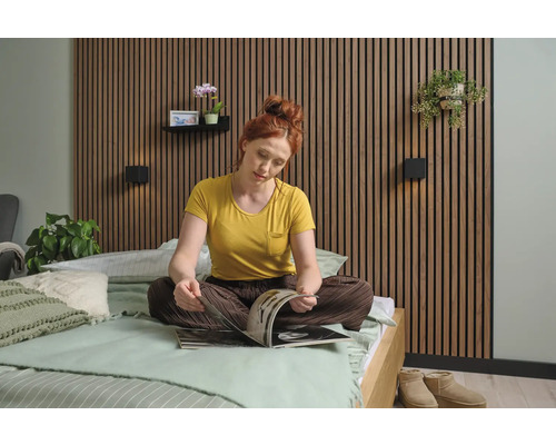 En kvinna sitter på en säng framför en väggbeklädnad och läser en tidning. Sovrummet är ljust och vänligt inrett.