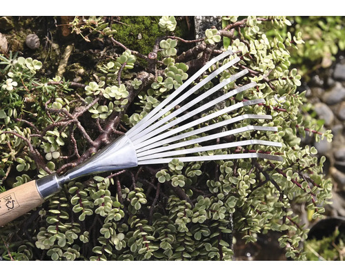 Metallräfsa med trähandtag framför gröna växter