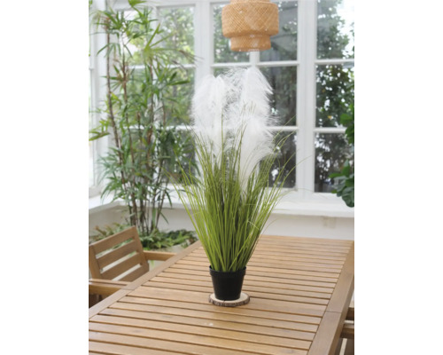 Dekorativ konstgjord växt med fjädrar i kruka på träbord