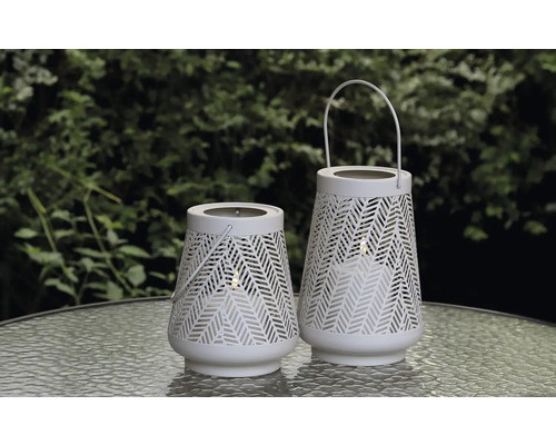 Två vita trädgårdslampor med mönster på ett bord