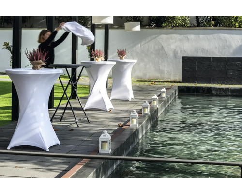 Miljö med ståbord, blomsterdekorationer och lyktor vid en damm