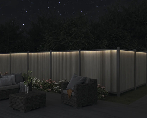 Trädgård med upplyst staket, sittgrupp och blommor på natten