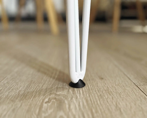 Närbild av ett vitt bordsben med golvskydd på ett trägolv.