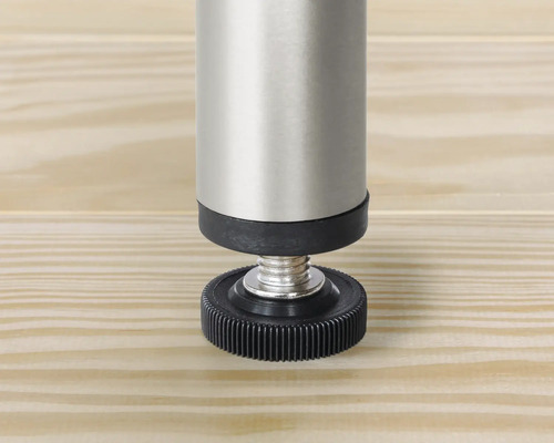 Detaljvy av ett justerbart möbelben i metall och plast på en träyta.