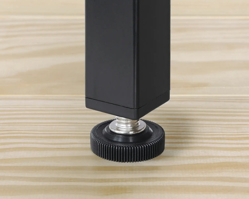 Detaljvy av ett svart bordsben med justerbar fot på ett trägolv.