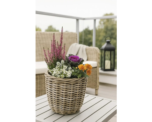 Dekorativa blommor och växter i en flätad korg på ett utomhusbord.