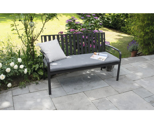 Trädgårdsbänk med kudde och tidning i trädgården